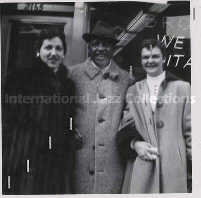 3 1/2 x 3 1/2 inch photograph. Lionel Hampton with two women, [in Canada]. Handwritten on the back of the photograph: Josi Bonomo (left), (Montreal); Joan Miller (right), (Montreal)