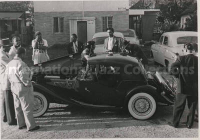 3 1/4 x 4 1/2 inch photograph. Gladys Hampton standing beside a car with some members of the Lionel Hampton's orchestra, which includes guitarist Billy Mackel