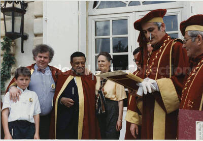 4 x 6 inch photograph. Lionel Hampton with unidentified persons, on the occasion of a ceremony related to wine, [in France]. Partially readable on the cover of a book held by a man are the words: [conf]rerie des Maitres; Table et du Vin