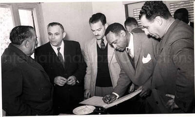 5 x 8 inch photograph. Gladys and Lionel Hampton with band in Israel. Lionel Hampton is signing a book with unidentified men
