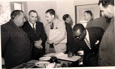 5 x 8 inch photograph. Gladys and Lionel Hampton with band in Israel. A member of the Lionel Hampton's band signing a book with unidentified men