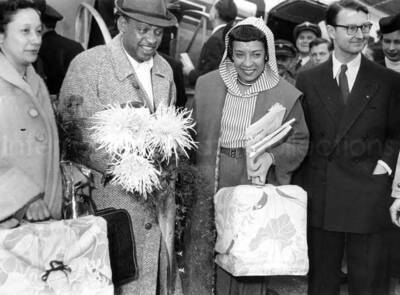 5 3/4 x 7 3/4 inch photograph. Gladys and Lionel Hampton with unidentified persons, walking outside an airport [in Germany?]