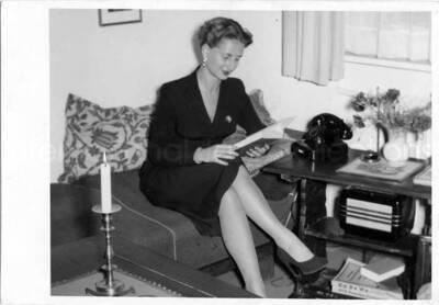4 x 5 1/2 inch photograph in the format of post card. Unidentified woman reading while sitting on a couch. A book on the table reads: Ka De We. Handwritten on the back of the photograph: Brigitte Tandsberg[?]; Berlin [Germany]