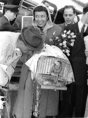 7 3/4 x 5 3/4 inch photograph. Gladys and Lionel Hampton with unidentified persons, walking outside an airport [in Germany?]