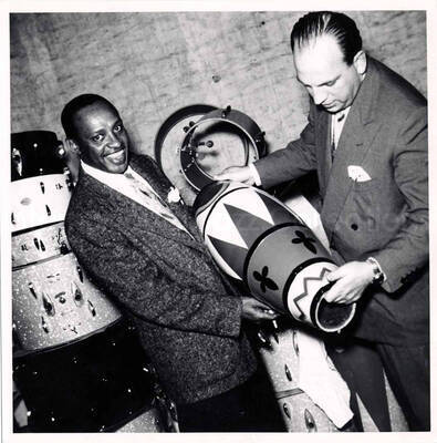 7 x 7 inch photograph. Lionel Hampton looking at various types of drums [in Germany?]
