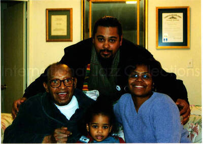 5 x 7 inch photograph. Lionel Hampton with a family in his apartment. Accompanying this photograph is a card of D. Kenneth Jenkins, freelance writer and radio program producer. Handwritten on the back of the card is a dedication to Lionel Hampton from Vashti Jenkins (Dinah Washington's Great Granddaughter) and family. This picture was in a connoisseur frame
