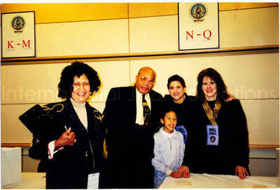 4 x 6 inch photograph. Unidentified persons standing up behind a table. The women are wearing identifications that read: Will call. The wall has signs with the 2001 Presidential Inauguration Seal, for President George W. Bush and Vice President Dick Cheney, indicating the alphabetical order of the names of the patrons