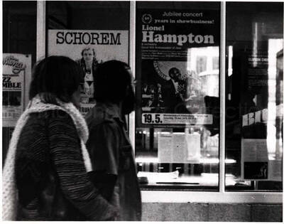 4 x 5 1/2 inch photograph. Pedestrians passing by a poster announcing Lionel Hampton jubilee concert. It reads: 50 years in show business; Lionel Hampton and Orchestra; Good Will Ambassador of Jazz [in German?]