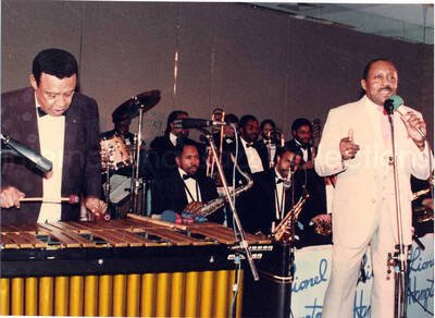 8 x 11 inch photograph. Lionel Hampton on vibraphone with band and unidentified man at the Charles Hotel, Boston. From a scrapbook