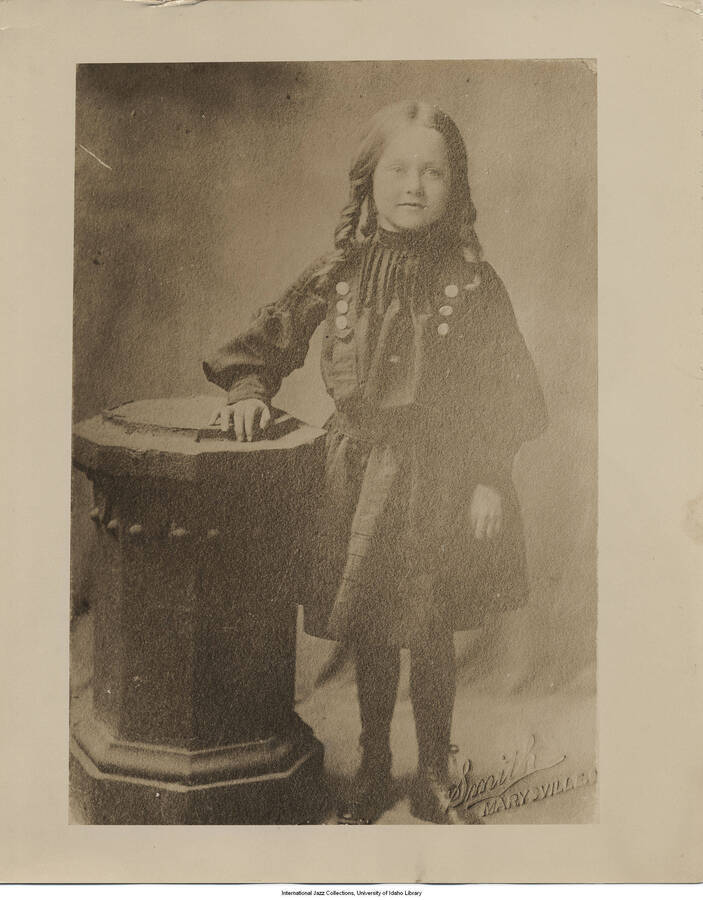 A young girl stands next to a table, possibly Lee Morse.