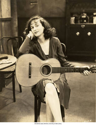 Black and white photograph of Lee Morse sitting and holding a guitar. Inscription: S-63-8