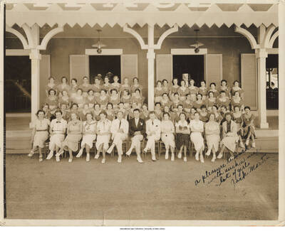 Black and white photograph of a group of people sitting in front of a building. Recto inscription: "A pleasure to work with such a nice lot of girls  Jack Martin". Verso inscription "Mrs. Robbie Peon, Pioneer Palace, August 6, 1936"