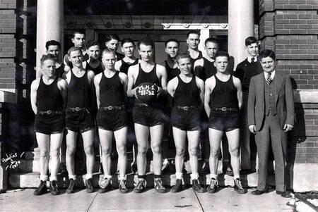 MHS basketball team and coach standing in group, black uniforms, holding basketball