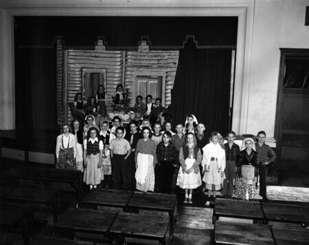 Students standing in costumes on a classroom stage