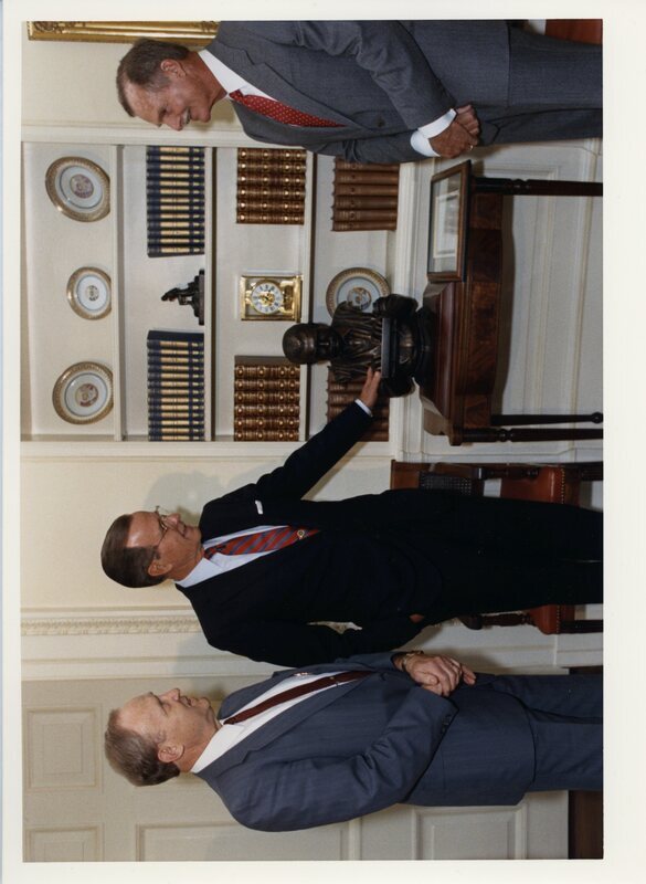 Photograph of Senator James A. McClure, President George H. W. Bush, and John "Jack" Hemingway, son of writer Ernest Hemingway, standing near a bust of Ernest Hemingway in the White House.