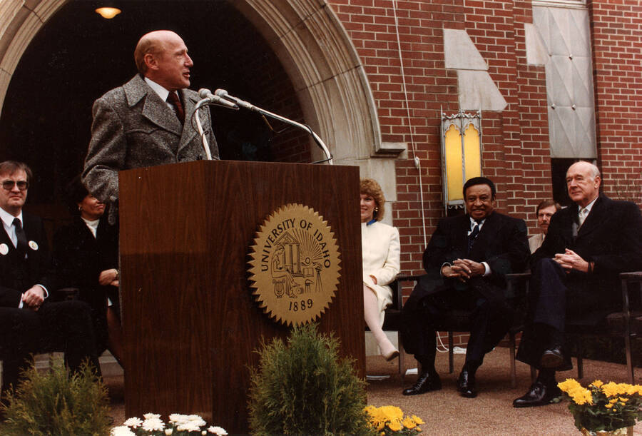 12" x 8" color photograph. President Richard D. Gibb speaking at the Lionel Hampton School of Music dedication. Lionel Hampton, Lynn "Doc" Skinner, Governor Cecil Andrus, Lynn St. James from Chicago, and an unidentified woman sitting in the background.