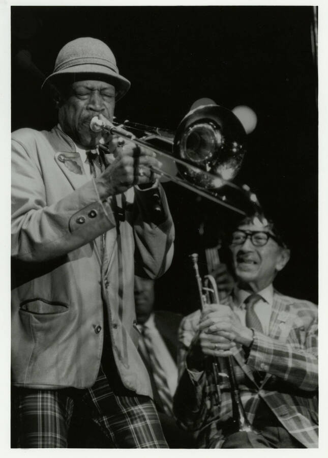 8" x 10" black and white photograph. Al Grey performing with Doc Cheatham sitting in the background looking on at the 1989 Lionel Hampton-Chevron Jazz Festival.