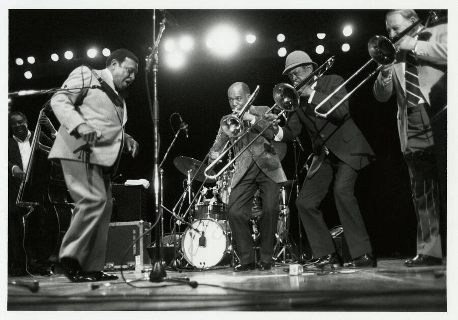7" x 5" black and white photograph. Lionel Hampton on stage with Al grey and two others playing trombones. Ray Brown plays the bass in the background.