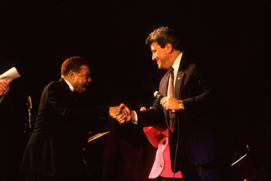 35 mm color slide. An unidentified man shakes Lionel Hampton's hand on stage  at the Pepsi International World Jazz Night at the 1992 Lionel Hampton-Chevron Jazz Festival. An unidentified woman claps in the background.