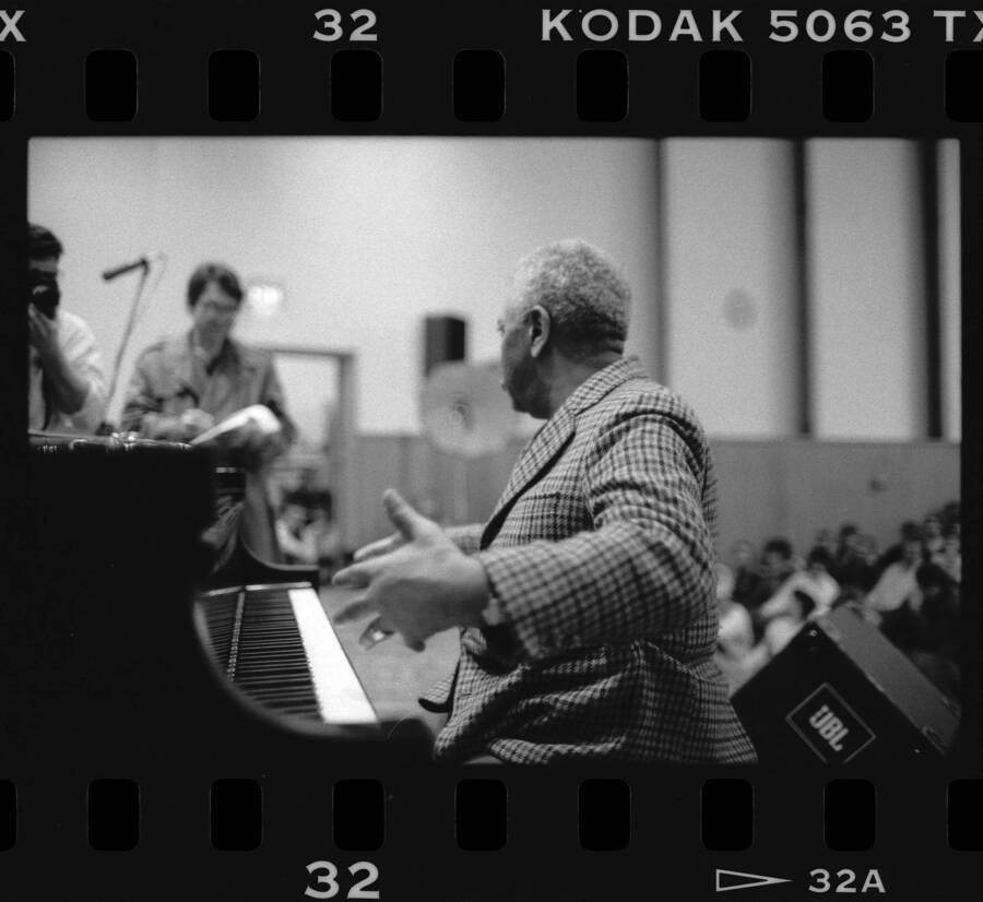 1.5" x 1" black and white print. One of thirty images found on a contact sheet. Dizzy Gillespie sitting at a piano while talking to a journalist.
