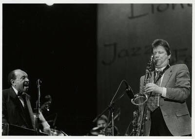 7" x 5" black and white photograph. Lionel Hampton watches Lembit Saarsalu as he plays the saxophone on stage at the Lionel Hampton Jazz Festival.