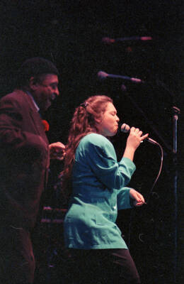 35mm color negative. A student vocalist performs at the 1991 Lionel Hampton-Chevron Jazz Festival evening concert while Lionel Hampton stands to the side.