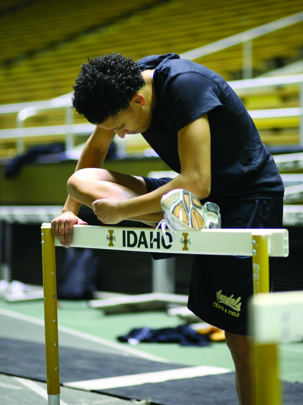 Color photograph of a runner stretching her leg atop a running hurdle that reads "IDAHO".