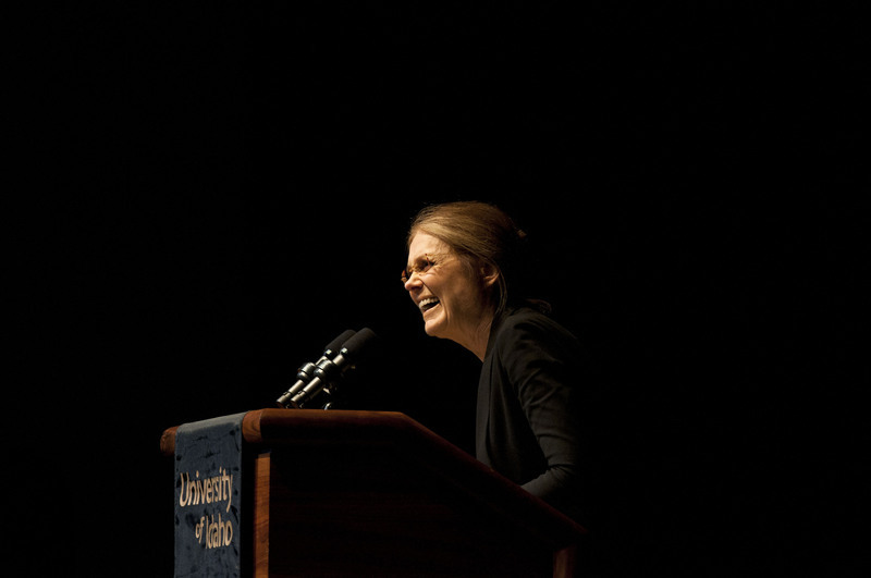 Color photograph of a woman standing at a podium with a drape that reads "University of Idaho".