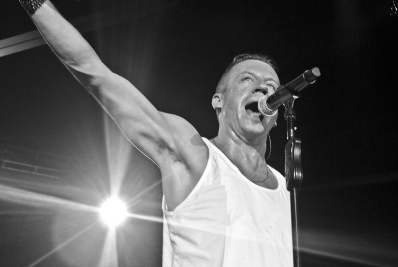 Black and white photograph of a man in a white tank top speaking or singing into a microphone.