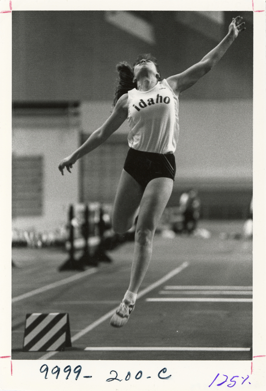 Black and white photograph of a woman in midair, her head thrown back and her arms outstretched. Her shirt reads "idaho".