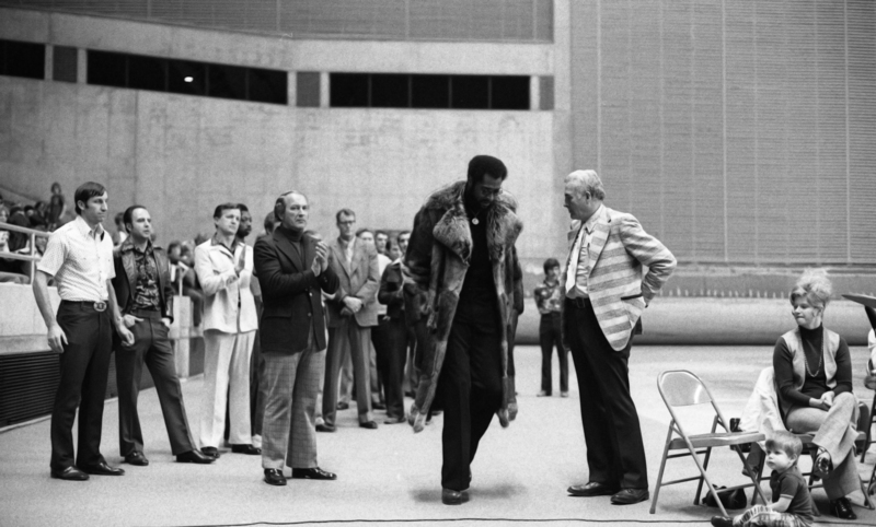 Black and white photograph of several people standing on the field of an enclosed stadium.