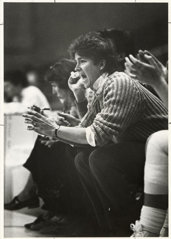 Black and white photograph of a woman sitting on the sidelines of a sports event.