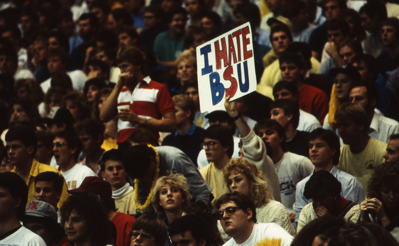 Color photograph of spectators sitting in stands. One holds a piece of paper that reads "I HATE BSU".
