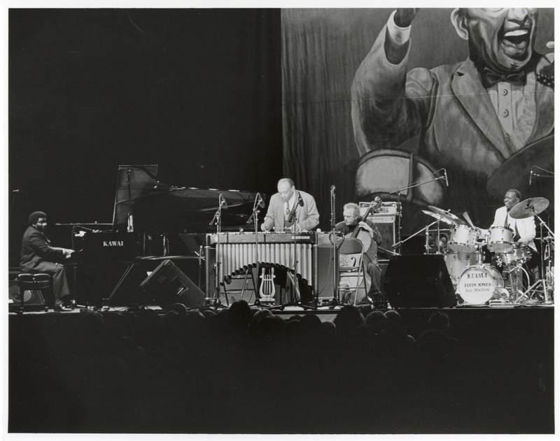 Black and white photograph of musicians playing on piano, vibraphone, bass, and drums on a stage.