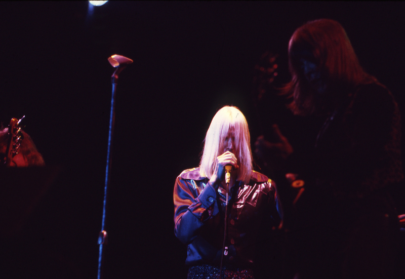 Color photograph of a man with white hair speaking or singing into a microphone.