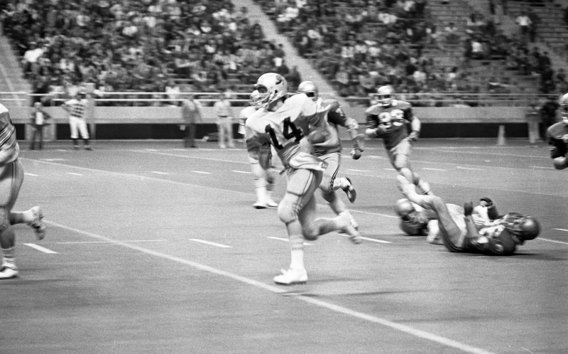 Black and white photograph of football players on a football field, with crowded stands in the background.