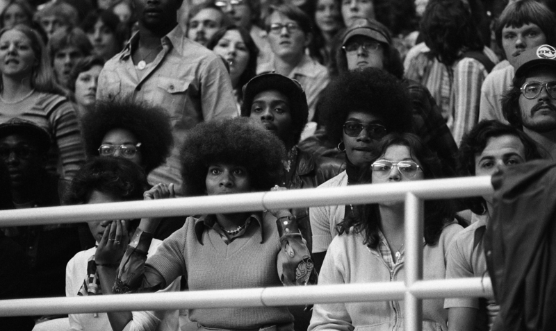 Black and white photograph of people sitting in stadium stands.