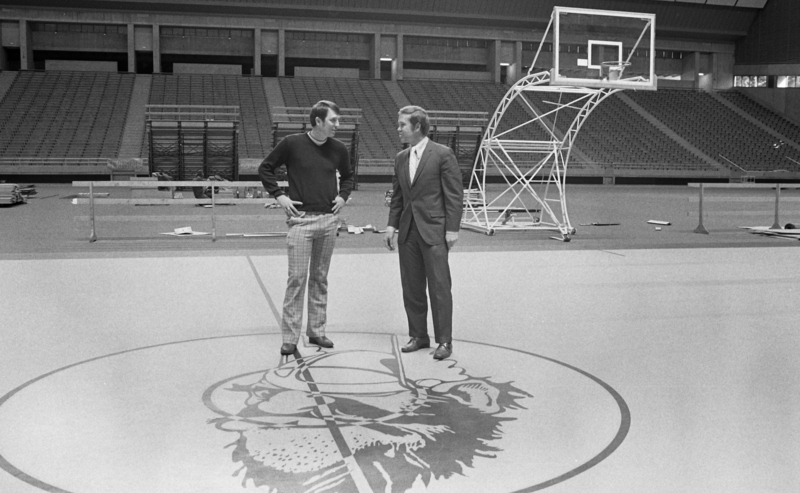 Two men stand next to each other on a basketball court.