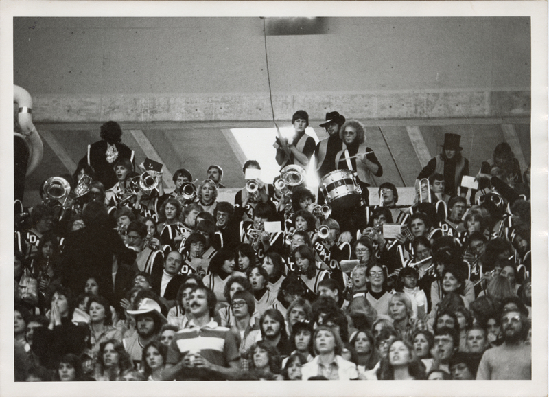 Black and white photograph of a marching band and spectators sitting or standing in stadium bleachers.