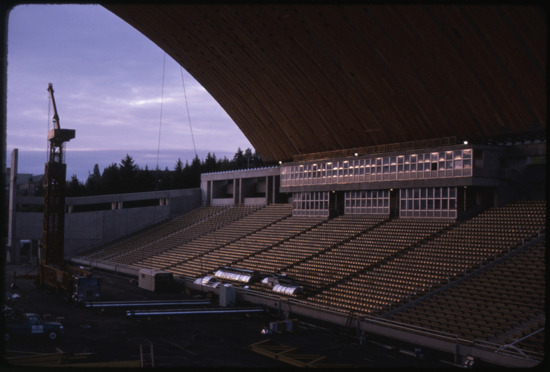 Color photograph of the interior of an arched stadium building under construction. Construction equipment sits on the field of the stadium.