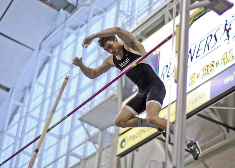 Color photograph of a pole vaulter going over the pole. He wears a black singlet.