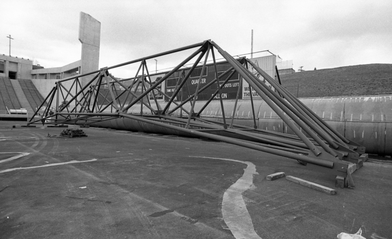 Black and white photograph of a metal truss sitting on the field of an open air stadium.