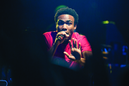 Color photograph of a man in a red shirt speaks or sings into a microphone.