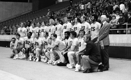 Black and white photograph of a group of people posing in rows for a photograph. In the background are stands.