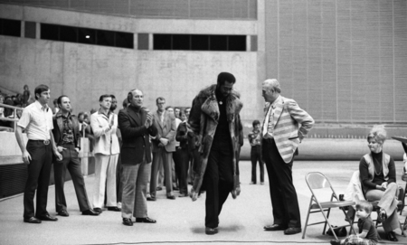 Black and white photograph of several people standing on the field of an enclosed stadium.