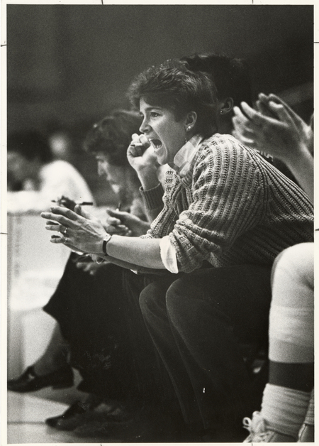 Black and white photograph of a woman sitting on the sidelines of a sports event.