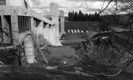 Black and white photograph of a building construction site. A concrete wall sits next to a dirt lot.