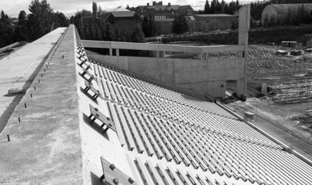 Black and white photograph of concrete stadium stands. In the background is construction equipment and more buildings.