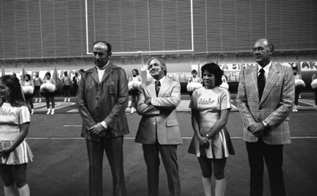 Black and white photograph of five people standing next to each other, football goalposts in the background.