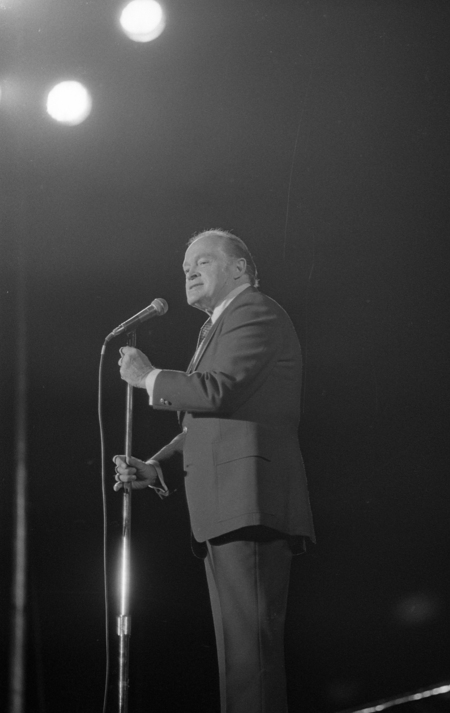 Black and white photograph of a man in a suit speaking into a photograph.